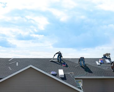 4 construction workers fixing roof against clouds blue sky, install shingles at the top of the house. Renovate, improvement, build home exterior by professional teamwork. Safety and protection concept