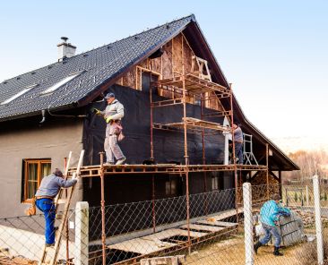 Construction workers standing on scaffold thermally insulating house facade with glass wool and black foil.