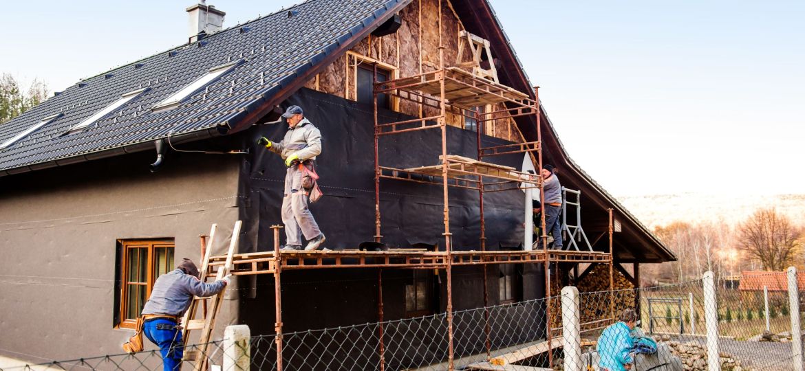 Construction workers thermally insulating house with glass wool